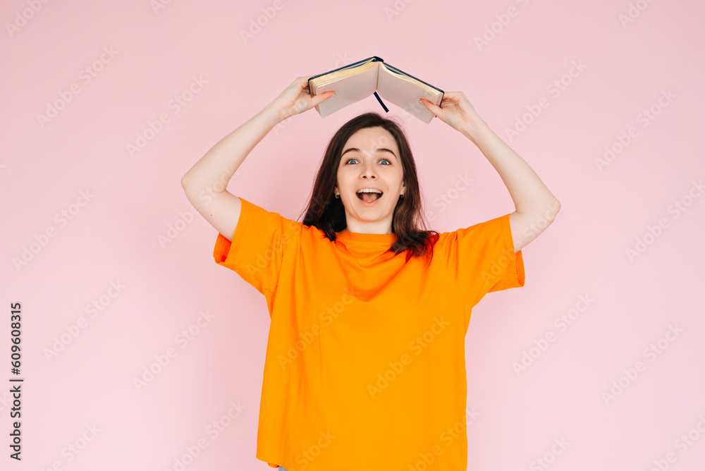 Joyful Book Enthusiasm: Cheerful Woman Holding Book Overhead with Exuberance - Delightful Mood and Positivity Concept, Isolated on Pink Background