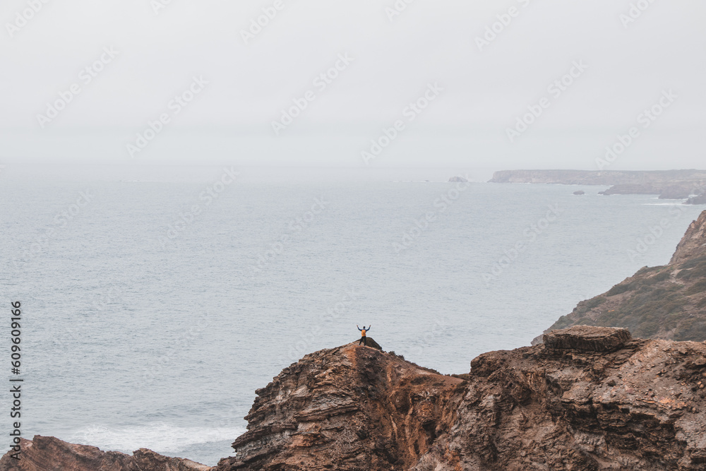 Adventurous man standing on the edge of a cliff enjoys the view of the 