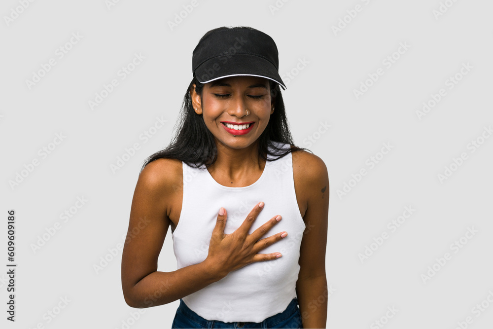 Young Indian woman cut out isolated on white background laughs out loudly keeping hand on chest. Young Indian woman cut out isolated on white background laughs out loudly keeping hand on chest.