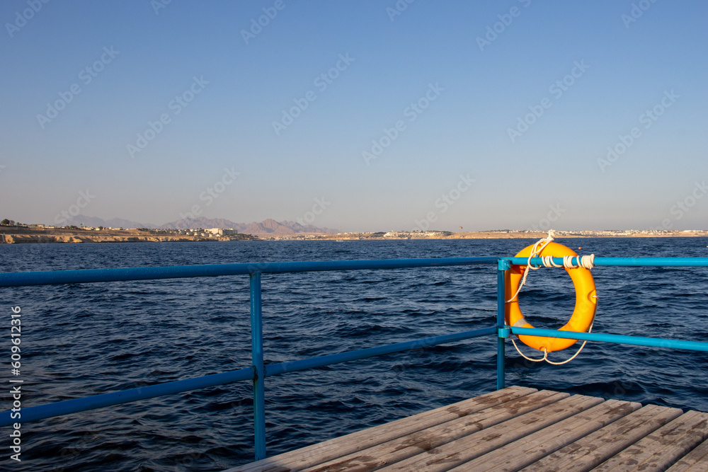 orange life buoy with blue railing and a dark blue sea