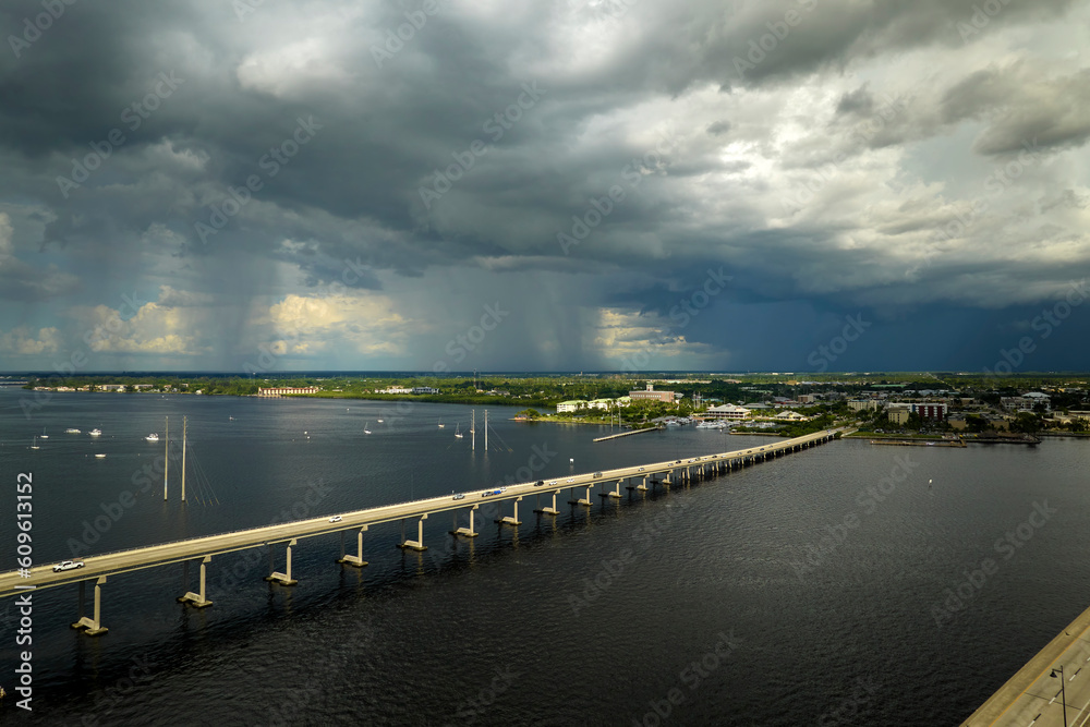 Heavy thunderstorm approaching traffic bridge connecting Punta Gorda and Port Charlotte over Peace River. Bad weather conditions for driving during rainy season in Florida