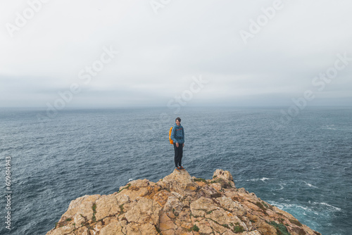 Black-haired adventurer stands at the end of Cape Cabo de Sao Vicente in the southwest of Portugal in the Algarve region. Man is enjoying his freedom. Wandering of Fisherman Trail