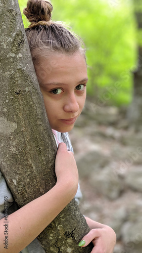 Teenage girl being shy and hugging a young tree