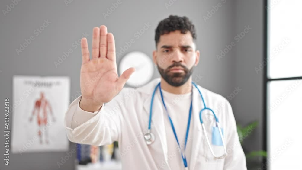 Young hispanic man doctor doing stop sign with hand at clinic Young hispanic man doctor doing stop sign with hand at clinic