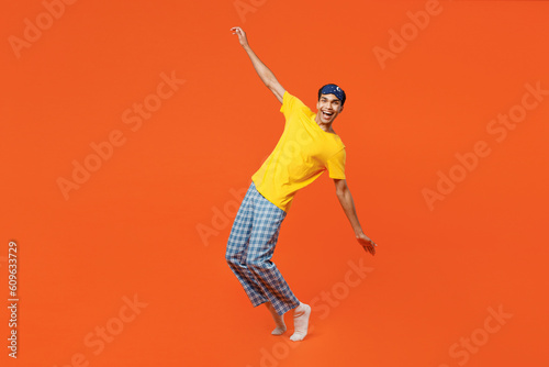 Full body young man wear pyjamas jam sleep eye mask rest relax at home stand on toes with outstretched hands lean back isolated on plain orange background studio portrait. Good mood night nap concept. © ViDi Studio