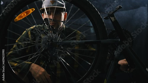 Wallpaper Mural A cyclist repairs a bicycle in a dark smoke-filled garage. A man in a shirt and baseball cap spins the wheel of a mountain bike and looks for faults Torontodigital.ca