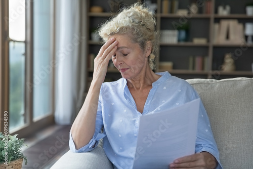 Upset senior elder woman shocked about health problems, financial crisis, holding paper documents, bank bankruptcy eviction notice, medical test result, touching head in stress