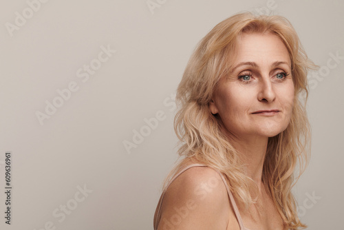 Beautiful blond middle aged woman smiling face looking sideways portrait. Elegant mature lady no makeup 50 years old close-up isolated on white studio. Women's health, cosmetology, skin care concept
