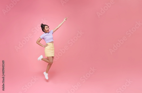 Happy Asian woman smiling jumping and pointing finger presenting to copy space isolated over pink studio background.