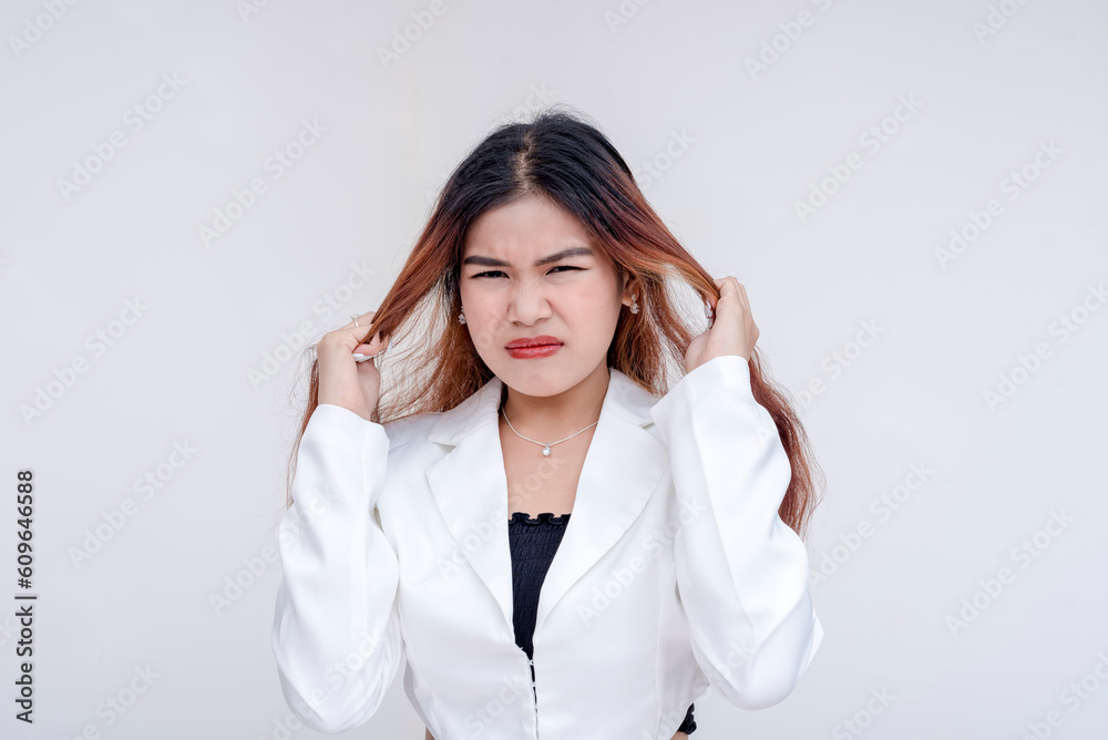 A frustrated and irritated young woman pulling her hair with both hands in annoyance. Isolated on a white background. A frustrated and irritated young woman pulling her hair with both hands in annoyance. Isolated on a white background.