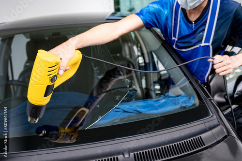 Auto specialist worker hand blowing hot air dryer or hairdryer removing old car window film tint and installing the new one. Car front windscreen film removal and tinting installation