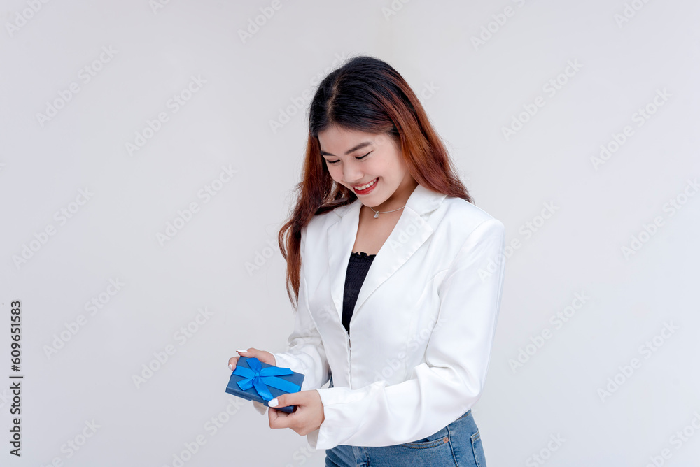 A happy and smiling young woman looking down at a small blue gift in her hands. Isolated on a white background. A happy and smiling young woman looking down at a small blue gift in her hands. Isolated on a white background.