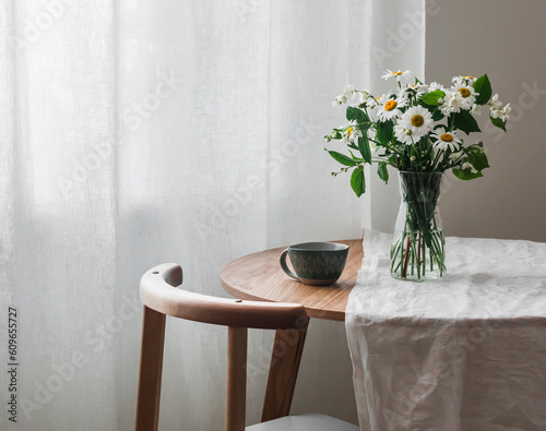 Slow morning - a cup on a wooden table with a white tablecloth and a vase with daisies and jasmine