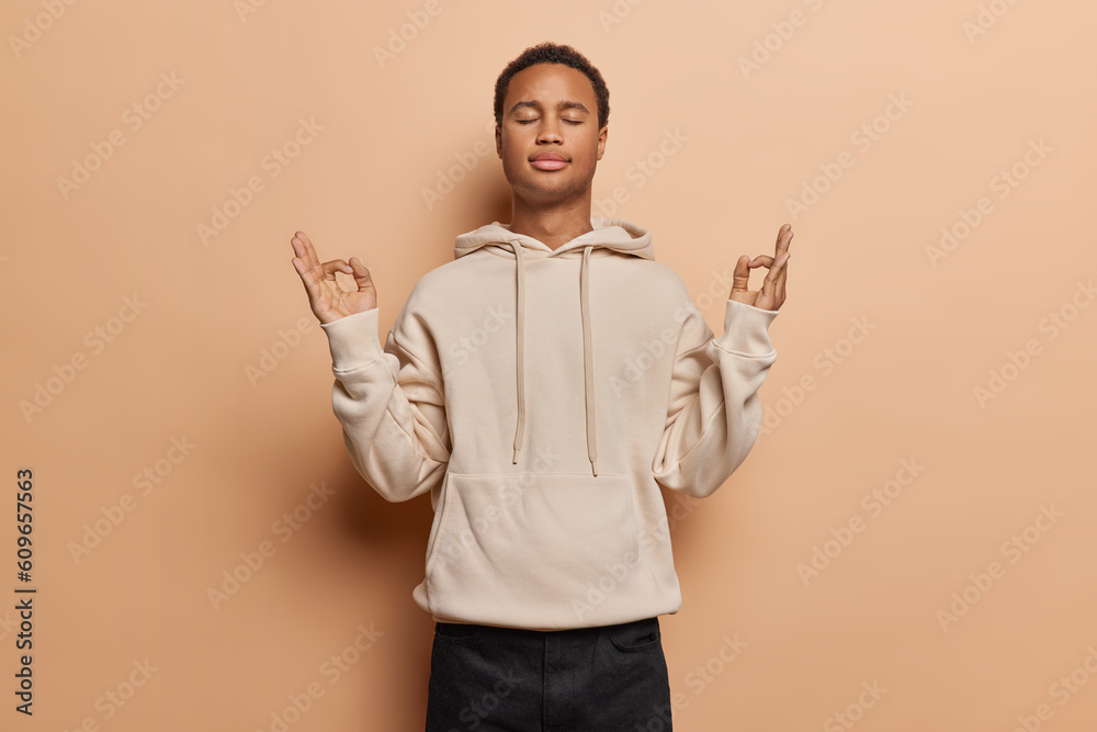 Tranquil young man exudes sense of calmness as peacefully closes his eyes practices mindful breathing and yoga captures essence of inner peace and relaxation dressed casually isolated over brown wall Tranquil young man exudes sense of calmness as peacefully closes his eyes practices mindful breathing and yoga captures essence of inner peace and relaxation dressed casually isolated over brown wall