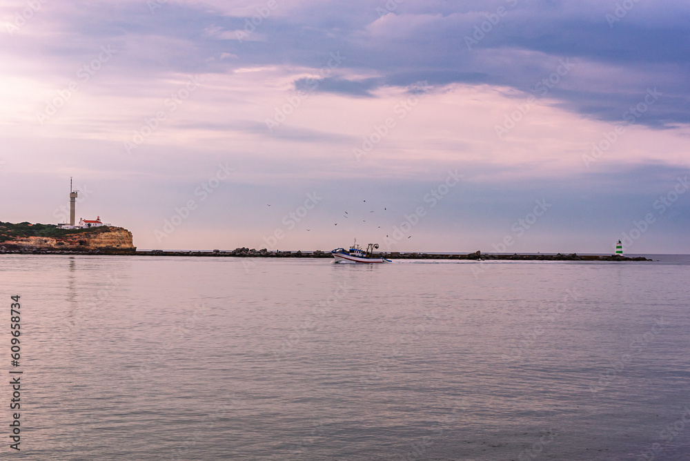 Lighthouse at Ponta do Altar,Ferragudo,with a fishing boat entering the ria.Algarve,Portugal.