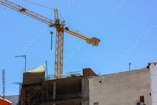 A yellow construction crane at a construction site against a blue sky. Construction business, real estate, construction of modern high-rise buildings. Real estate engineering.