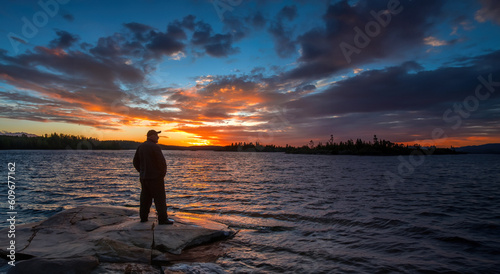 Sunset in Karelia. Nature Russia. Man admires sunset. Guy on seashore. Traveler with back to camera. Karelia on summer evening. Man stands on stone coast. Landscape Russia. Sunset over Karelia nature