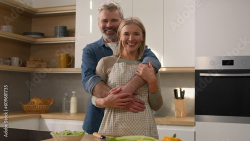 Loving happy family carefree couple adults middle-aged spouses senior man mature woman looking at each other smiling with love bonding affectionate homeowners hugging at kitchen cooking home portrait