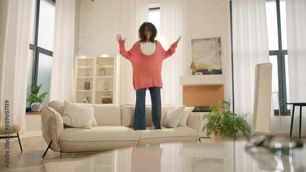 Afro girl homeowner having fun on move in day, celebrating mortgage approval, relocation to upgraded apartment. Bank mortgage concept. Excited happy young woman of color jumping happily on modern sofa Afro girl homeowner having fun on move in day, celebrating mortgage approval, relocation to upgraded apartment. Bank mortgage concept. Excited happy young woman of color jumping happily on modern sofa