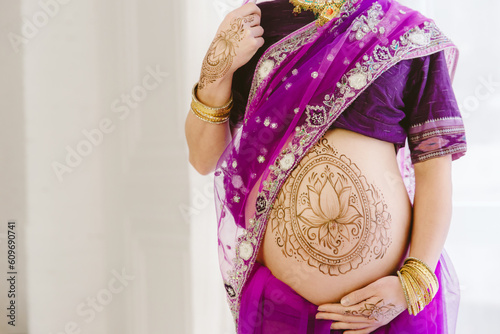 Pregnant woman in purple sari. mehendi. Indian painting on woman's hands and pregnant belly with henna tattoo on white room background