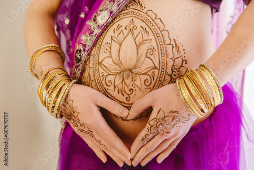 Pregnant woman in purple sari. mehendi. Indian painting on woman's hands and pregnant belly with henna tattoo on white room background