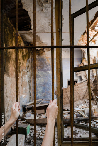 Hands holding onto the fence overlooking abandoned demolished house