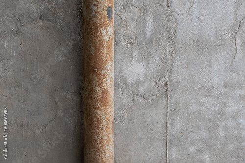Old rusty metal water pipe against a shabby concrete wall
