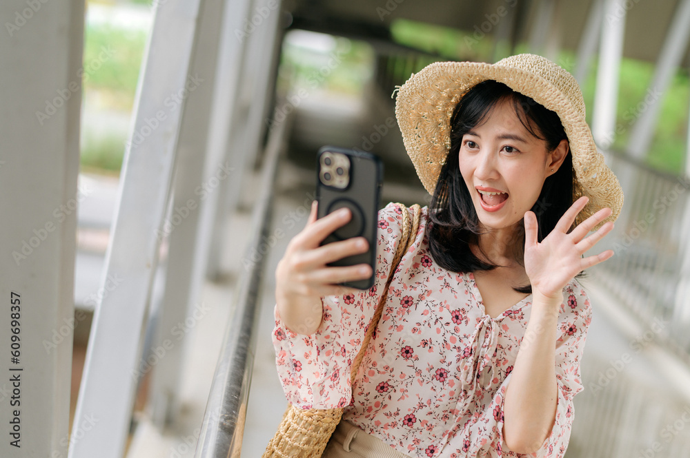 young asian woman traveler with weaving basket selfie with mobile phone and standing on overpass. Journey trip lifestyle, world travel explorer or Asia summer tourism concept.