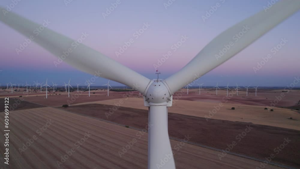 Aerial top view of a Close-up to a Windmill (zoom out) in Wind turbines Farm at sunset. Numerous windmills rotating in the background. Cuenca, Castilla La Mancha, Spain