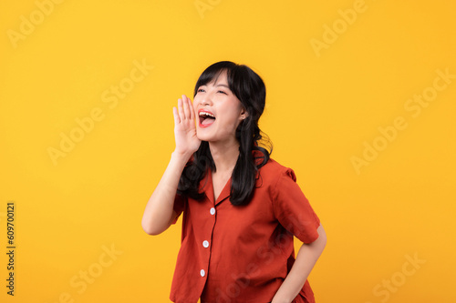 Fotografia Portrait young beautiful asian woman happy smile dressed in orange clothes shout to free space isolated on yellow studio background