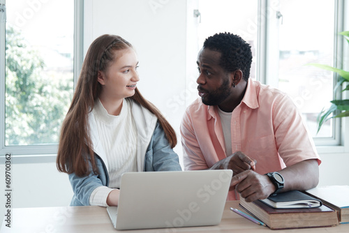 Young African teacher or tutor is teaching for knowledge about online homework with internet on laptop for Caucasian student girl in classroom. Education and Technology for homeschool Concept.