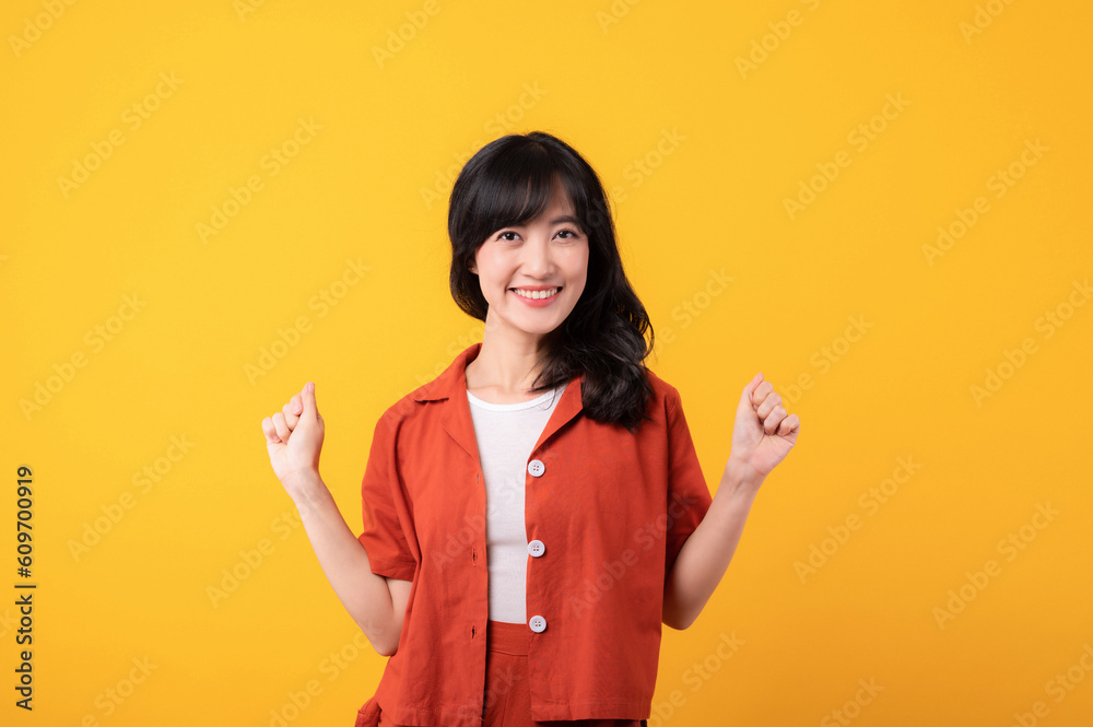 Portrait young beautiful asian woman happy smile dressed in orange clothes showing fist up hand gesture isolated on yellow studio background. Successful hooray celebrate young person concept. Portrait young beautiful asian woman happy smile dressed in orange clothes showing fist up hand gesture isolated on yellow studio background. Successful hooray celebrate young person concept.