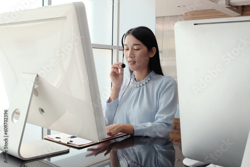 Smiling asian woman is call center or secretary operator is wearing a headset and a microphone for consultant to customers. Technician Support staff for advise and help resolve technical issues.
