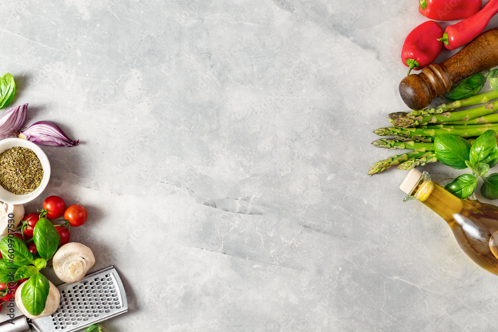 Food cooking ingredients background with fresh vegetables, herbs, spices and olive oil on white stone table top view. Healthy vegetarian eating