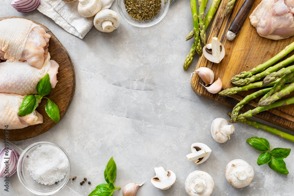 Frame of fresh pieces of chicken thigh meat on wooden cutting board with ingredients for cooking healthy food on light background top view