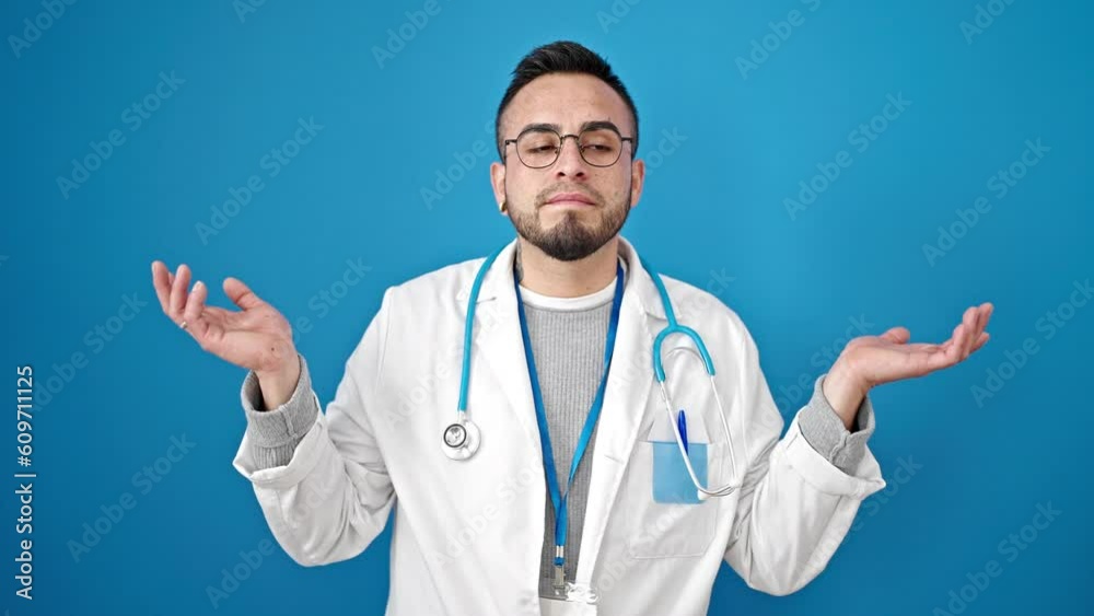 Hispanic man doctor standing clueless over isolated blue background Hispanic man doctor standing clueless over isolated blue background
