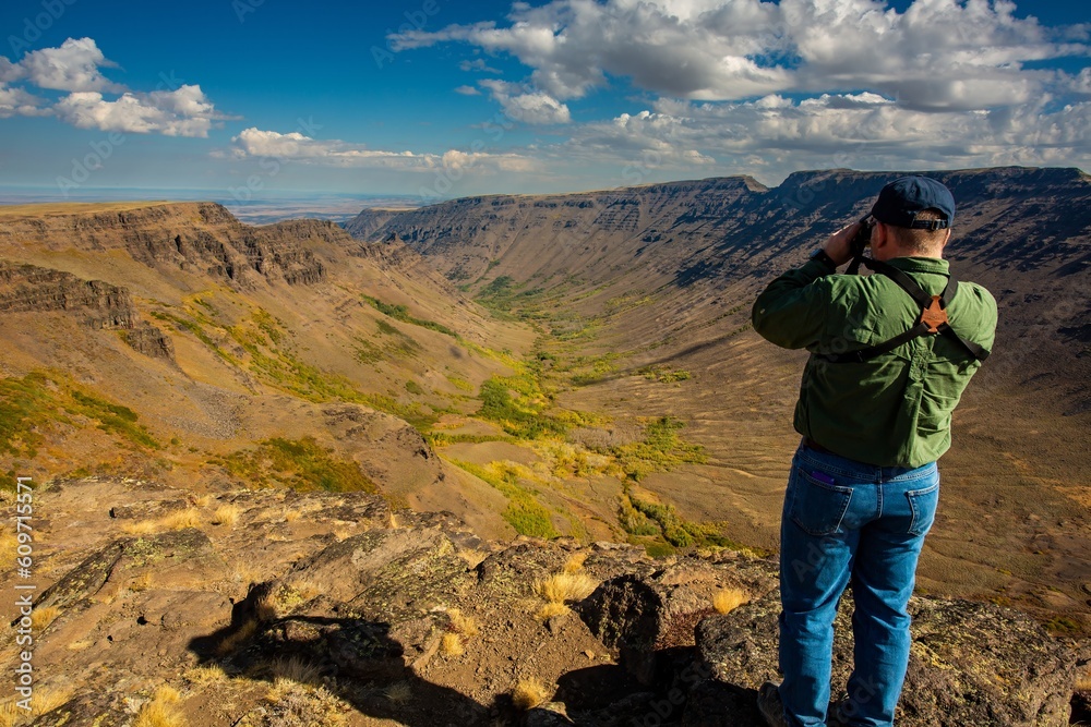Steens Mountains, Oregon - 9/20/2018: A man, looking east through binoculars, standing at the top of Keiger gorge in the steens mountains, near Frenchglen, Oregon. Steens Mountains, Oregon - 9/20/2018: A man, looking east through binoculars, standing at the top of Keiger gorge in the steens mountains, near Frenchglen, Oregon.