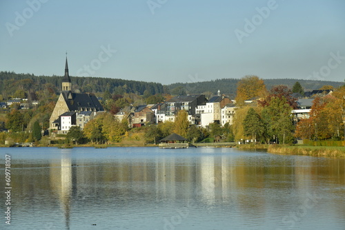 Le lac des Doyards et le village de Vielsalm avec l'église paroissiale Saint Gengoux se reflétant dans ses eaux  sous un ciel clair d'automne  photo