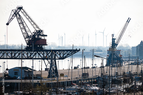 City harbor on the Warnow River in Rostock in Germany. With harbor quay, cranes, boats, wind turbines and warehouses.
