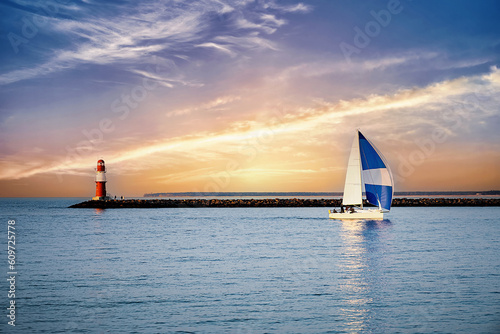 Fototapeta Naklejka Na Ścianę i Meble -  Sailing ship off the coast of the Baltic Sea with a red lighthouse and spectacular sky features of sunshine and clouds.