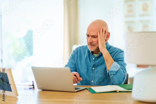 Mid aged man sitting at desk at home and using laptop for work