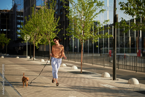 Young pretty female adult with small ginger dog in the bi city walking having fun. City view High quality photo