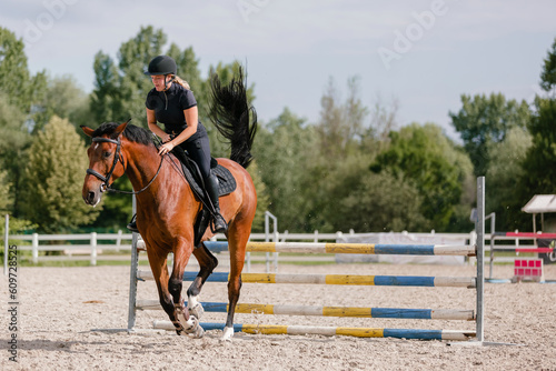 Female rider on chestnut horse jumping over a hurdle at the equestrian center on a sunny summer day. Equitation sport concept. © 24K-Production