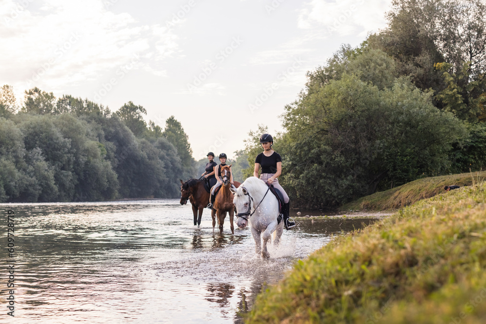 Three girls relaxing in a natural setting, horseback riding across the river during sunset. Outdoors activity and active lifestyle concept. Three girls relaxing in a natural setting, horseback riding across the river during sunset. Outdoors activity and active lifestyle concept.