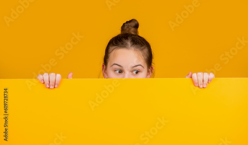 kid hiding behind blank yellow paper with copy space for advertisement