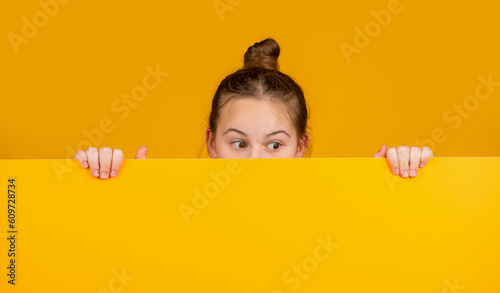 kid hiding behind blank yellow paper with copy space for advertisement photo