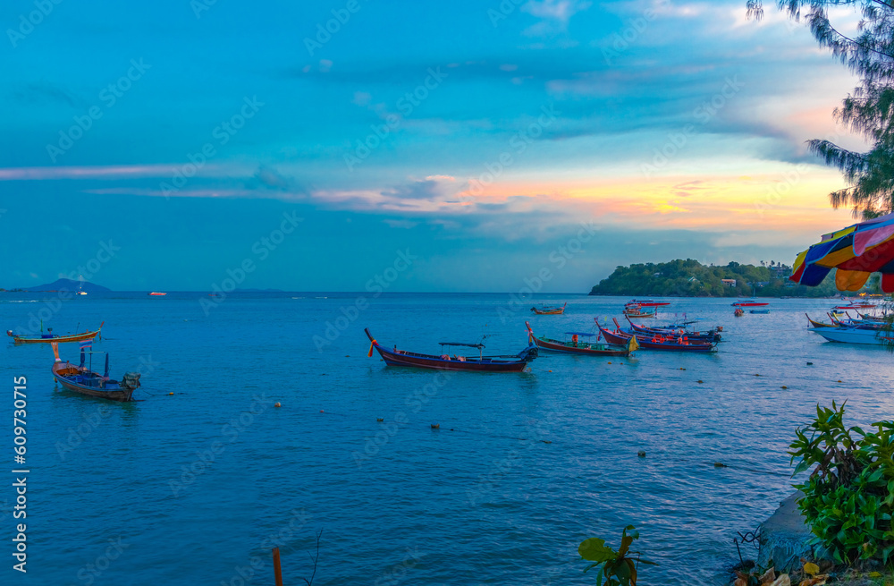 Colourful Skies Sunset over Rawai Beach in Phuket island Thailand. Lovely turquoise blue waters, lush green mountains colourful skies and beautiful views the pier and longtail boats and islands 
