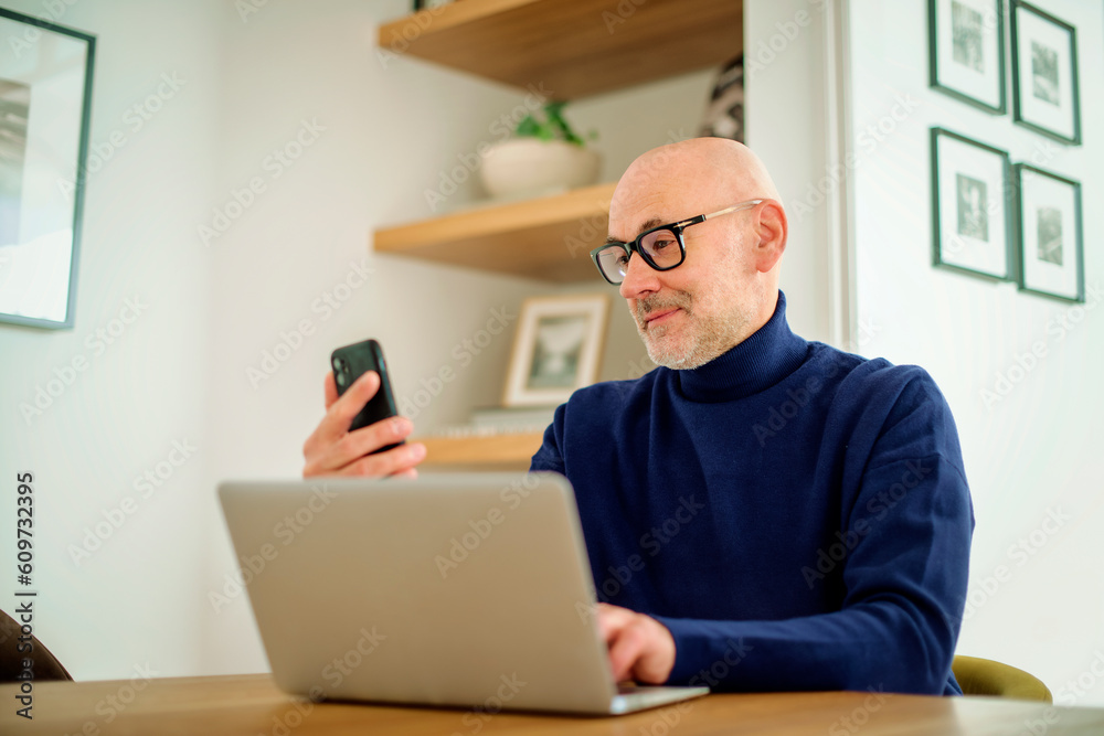 Middle aged businessman using smartphone and laptop while working from home
