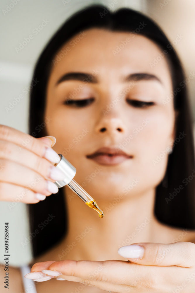 Attractive girl with drop of essential oil in pipette in hands close-up. Young woman is applying moisturizing serum on her skin. Attractive girl with drop of essential oil in pipette in hands close-up. Young woman is applying moisturizing serum on her skin.
