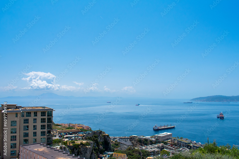 Naklejka premium Gibraltar, Aerial view on buildings, city and coast of sea. Crystal clear blue water against mountains